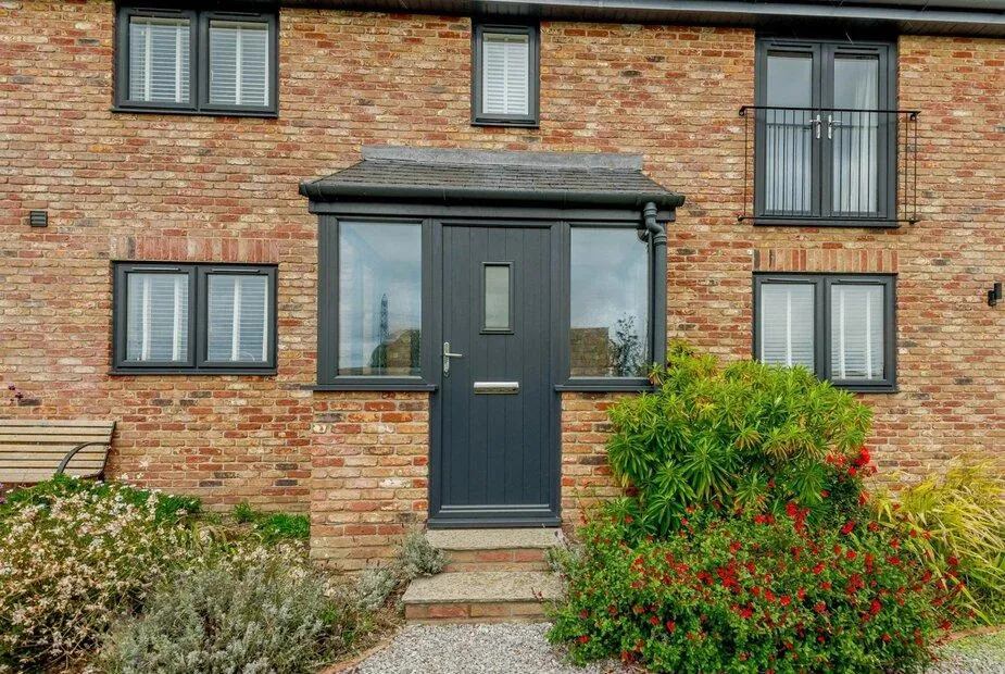 Brick frontage of Cottage with grey door and shrubs in the garden