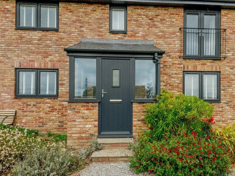 Brick frontage of Cottage with grey door and shrubs in the garden
