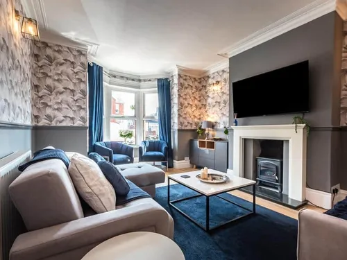 Cottage living room with fireplace, wall-mounted TV, and bay window with blue chairs