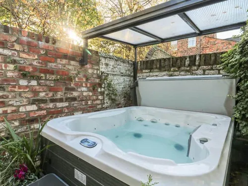 Cottage garden with covered hot tub next to brick wall