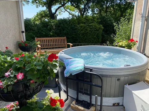 Cottage patio with round hot tub, wooden bench and potted flowers
