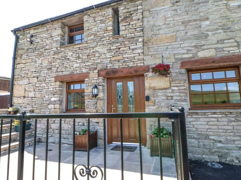 Stone exterior of Birkett Barn with wooden door, iron gate, and flower planters visible.