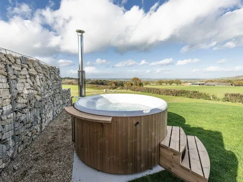 Lodge garden with round wooden hot tub and stone wall, overlooking countryside