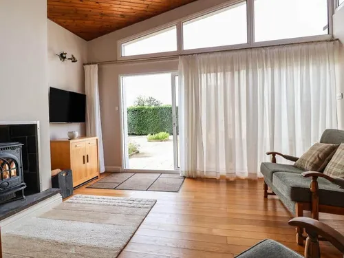 Lodge living room with wood burner, sofa and patio door with garden view