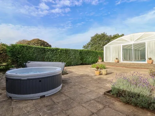 Patio at lodge with hot tub and potted plants near hedge and glazed outbuilding