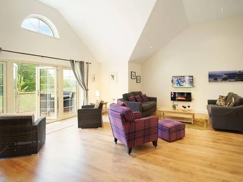 Lodge living room with sofas, armchairs, TV and patio doors to decking area