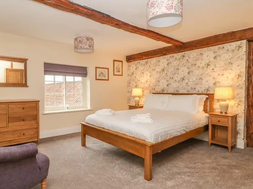 Cottage bedroom with double bed, floral wallpaper and exposed wooden ceiling beams