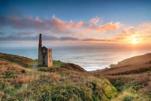 Golden sunset over the historic Rinsey Head engine house in Cornwall, sitting on a cliff edge overlooking the Atlantic Ocean