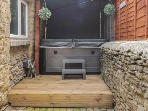 Cottage patio area with hot tub and wooden steps enclosed by stone walls