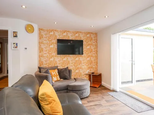 Cottage lounge with wall-mounted TV, round chair and patio doors to outside seating area