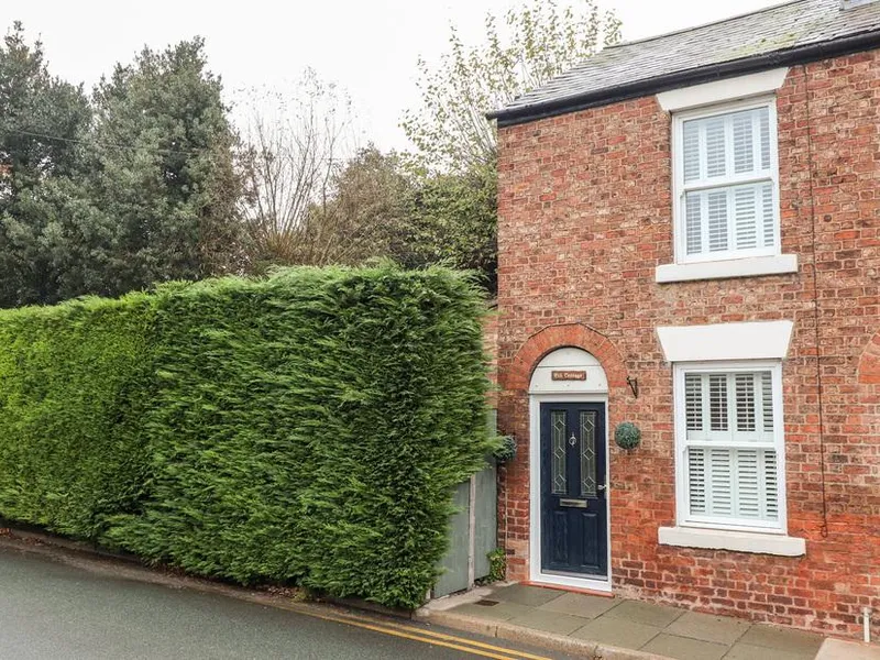 Elv Cottage brick exterior with tall hedge and white window shutters