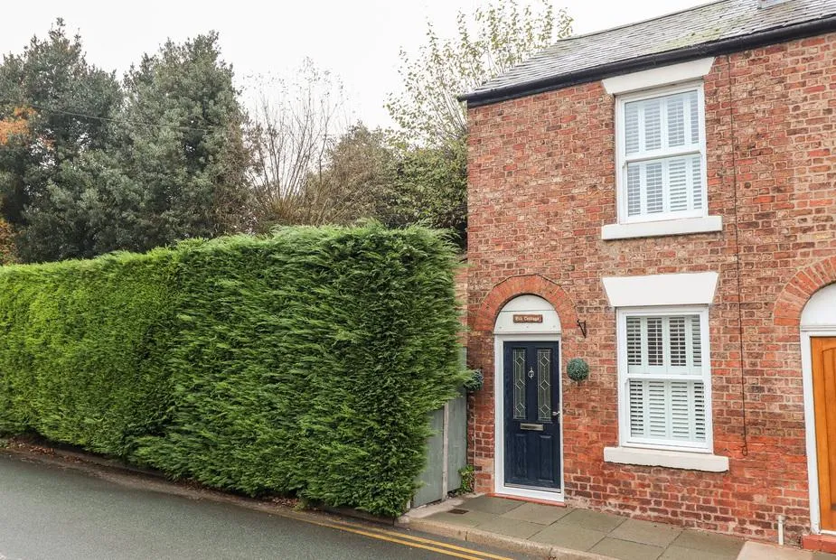 Elv Cottage brick exterior with tall hedge and white window shutters