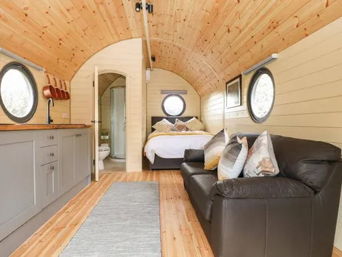 Lodge interior with sofa, bed and kitchenette, round windows and wood-panelled ceiling