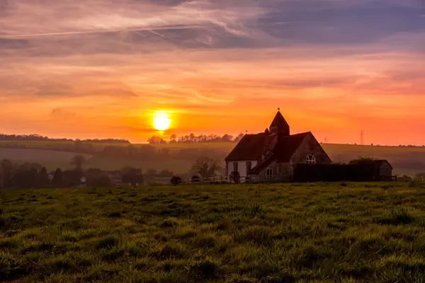 Sunset glowing over the historic St Hubert's Church in the rolling South Downs of Hampshire.