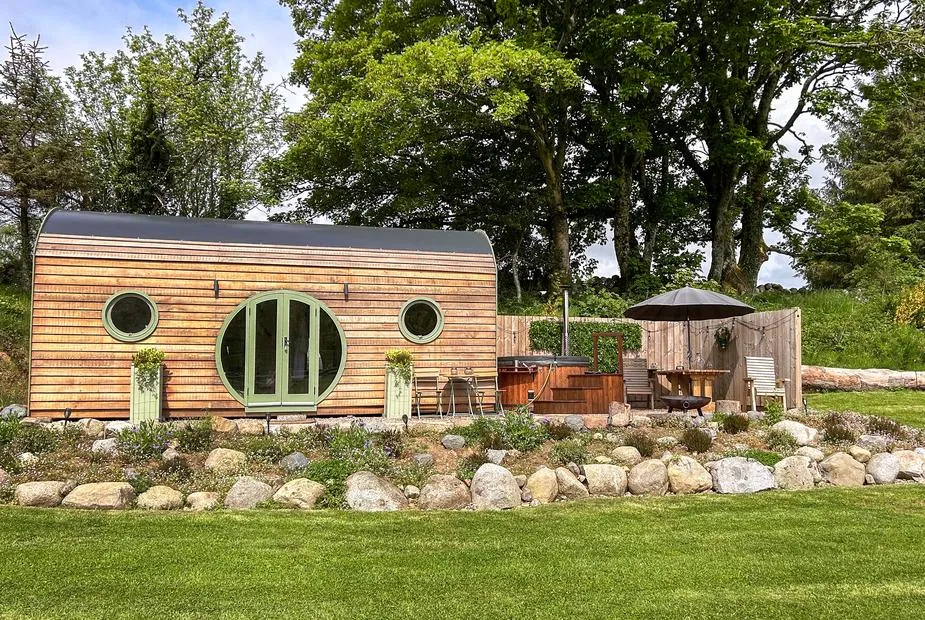 Heather lodge with round windows and outdoor hot tub in a garden setting
