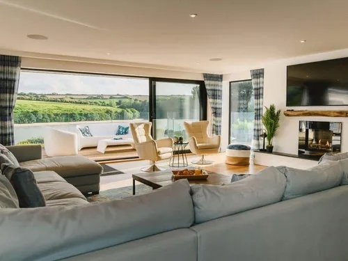 Cottage lounge with corner sofa, fireplace and large windows overlooking countryside