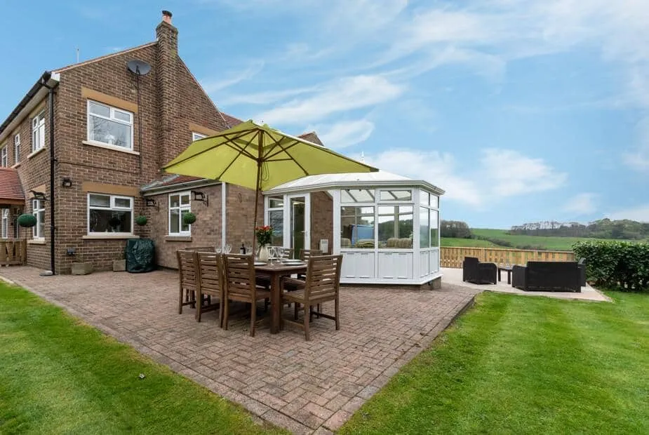 High Croft exterior with patio dining set, large parasol, and conservatory overlooking fields