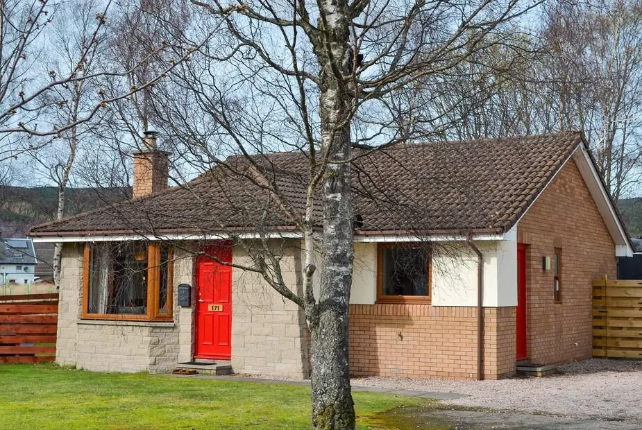 Holly Lodge exterior with red doors and a tree in the front garden