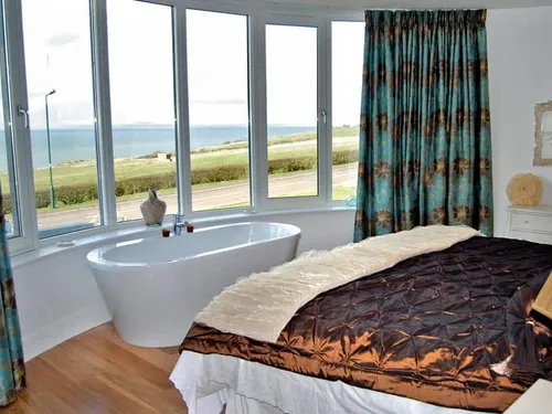 Cottage bedroom with freestanding bath beside bay window and sea view