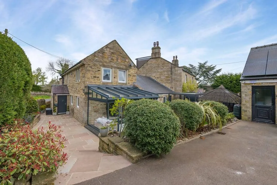 John's Cottage stone exterior with glass sunroom and landscaped garden shrubs