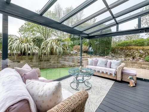 Cottage conservatory with wicker sofas and glass coffee table overlooking garden