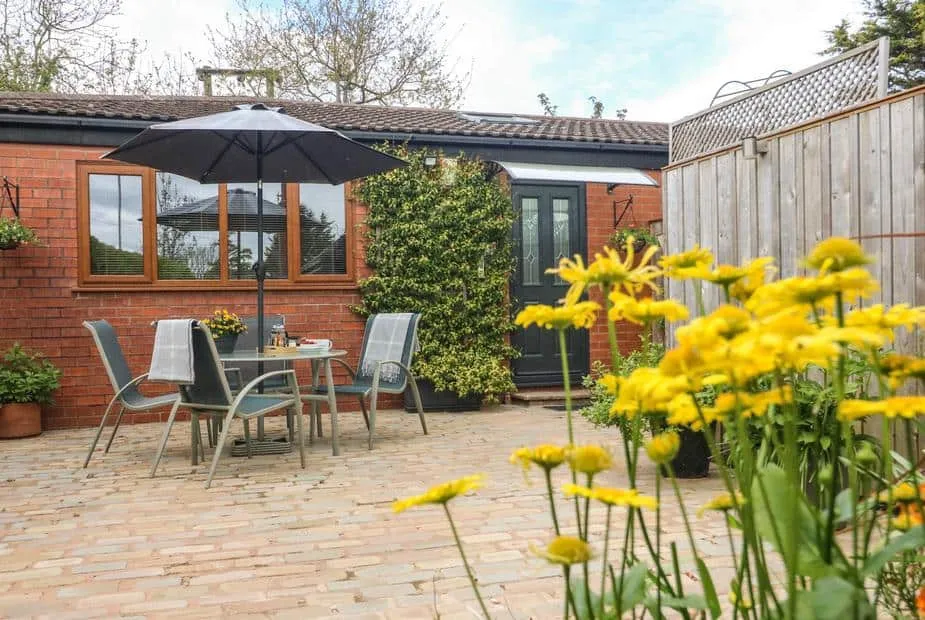 Kilmory Lodge brick patio with outdoor dining set, umbrella, and yellow flowers in foreground