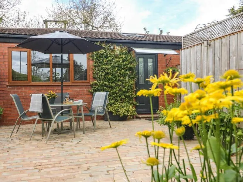 Kilmory Lodge brick patio with outdoor dining set, umbrella, and yellow flowers in foreground