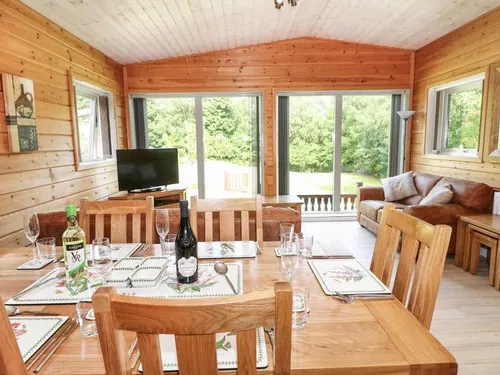 Lodge dining area with wooden table, TV, sofa and sliding glass doors to garden