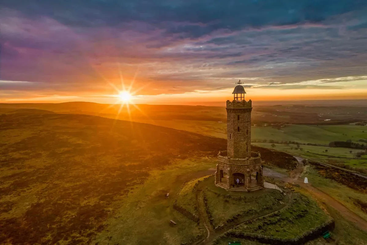 Golden sunset creates a dramatic sunburst behind Darwen Tower, overlooking the rolling Lancashire countryside.