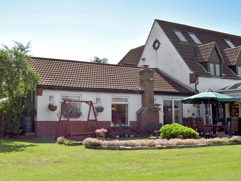 Leanda Lodge exterior with garden swing seat and patio dining area under a green umbrella