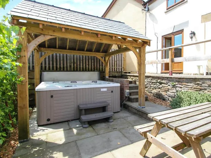 Lilly Cottage outdoor hot tub under wooden pergola with picnic bench nearby