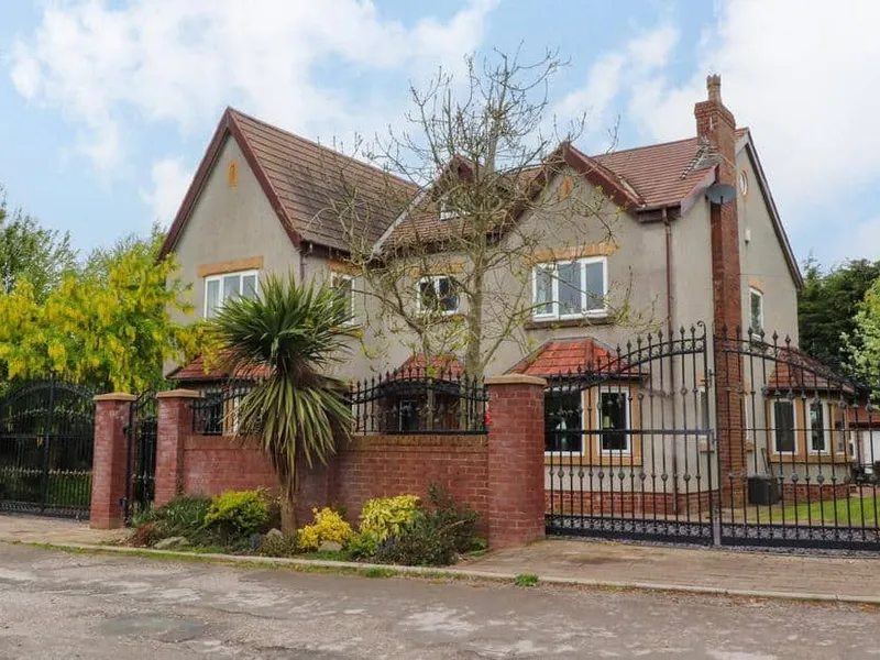 Linwood with red brick wall, wrought iron gates and front garden with palm tree.