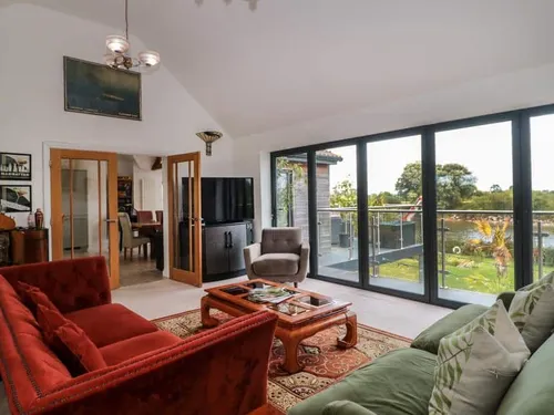 Cottage living room with large sofas and glass doors opening to balcony with garden view