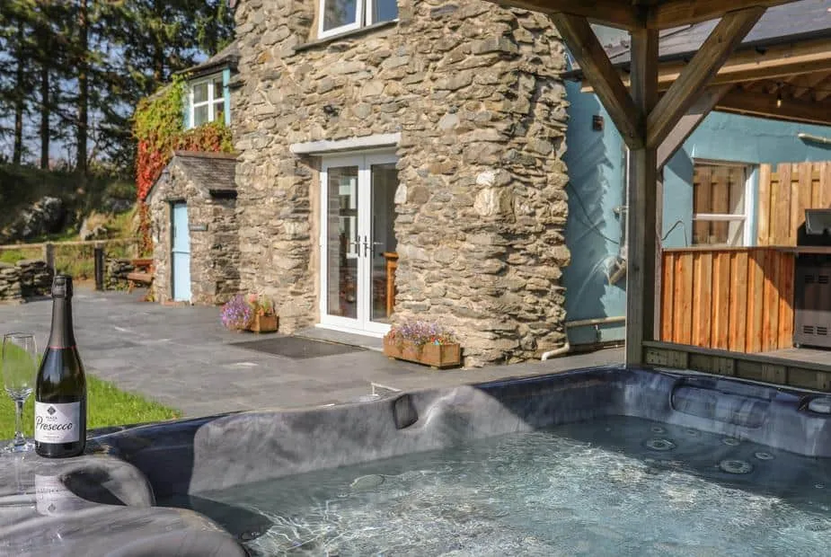 Stone cottage exterior with hot tub and Prosecco on the patio at Maes Madog.
