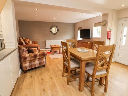 Open-plan cottage lounge and dining area with table, sofa, and TV unit
