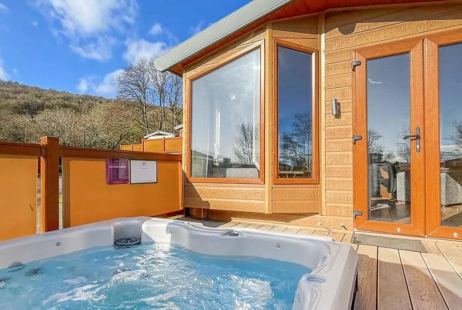 Mendip Premier with outdoor hot tub on wooden decking, large windows and hillside view