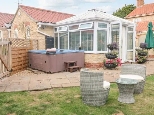 Cottage patio with hot tub, rattan chairs and glass-topped table in garden area