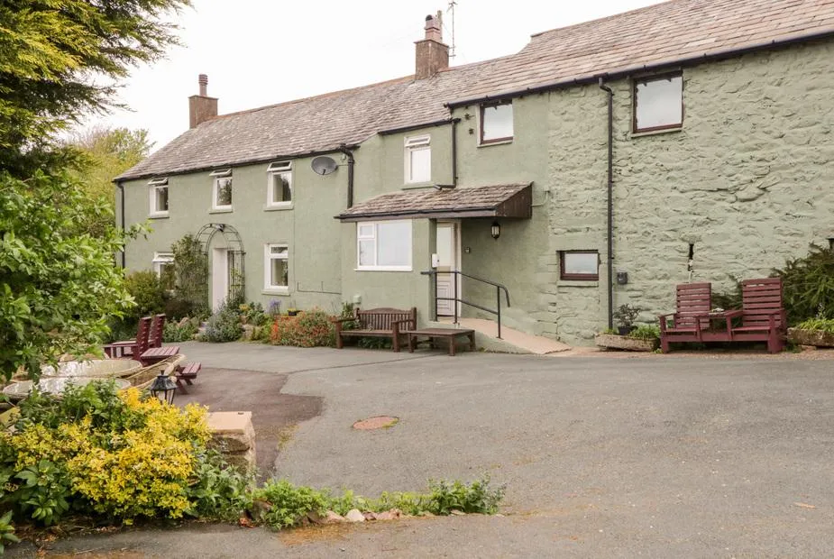 Near Bank Cottage exterior with stone walls and outdoor seating benches in front garden.
