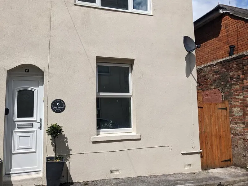 North Harbour House exterior with white door and window near brick wall and wooden gate
