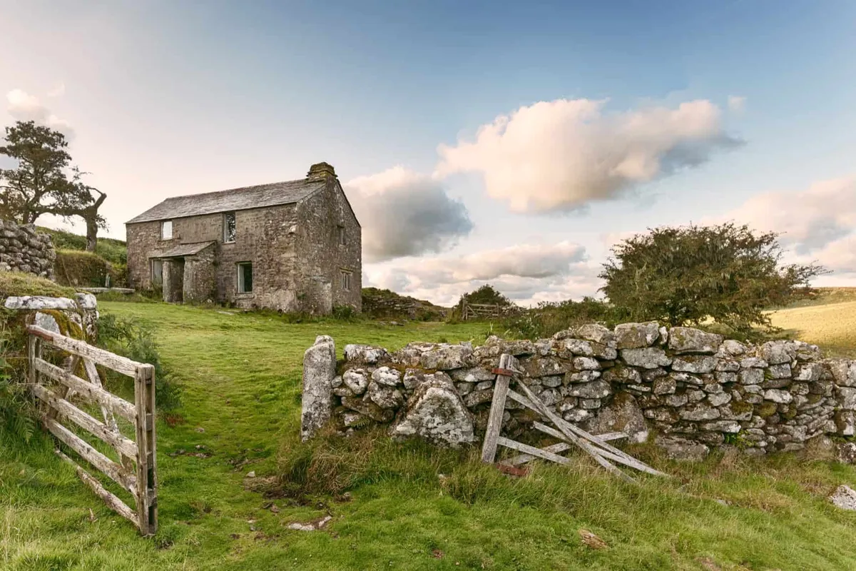 A remote stone farmhouse with a dry-stone wall set in the rugged, open moorlands of the North of England.