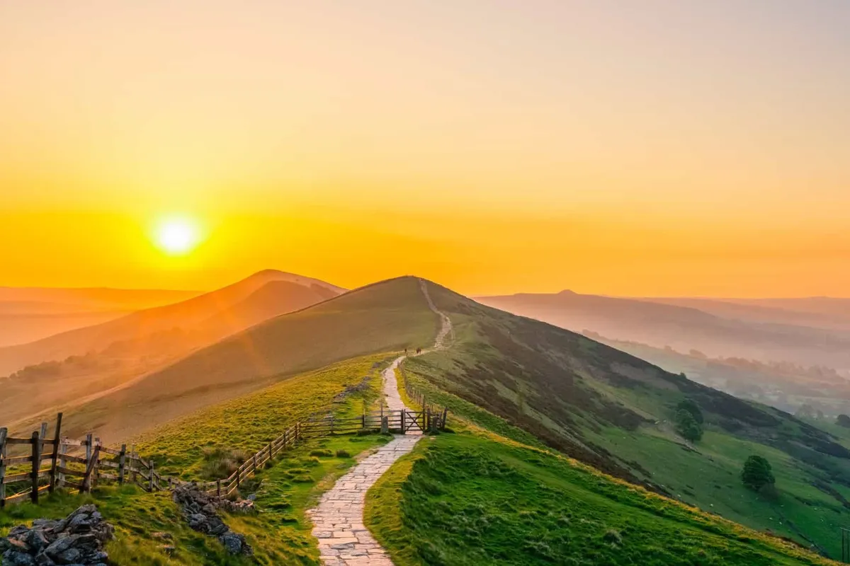 Golden sunrise sunburst shining over the stone path leading up to the summit of Mam Tor in the Peak District.