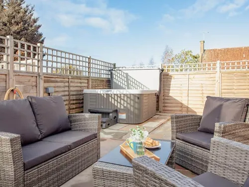 Patio with rattan seating and hot tub in fenced cottage garden
