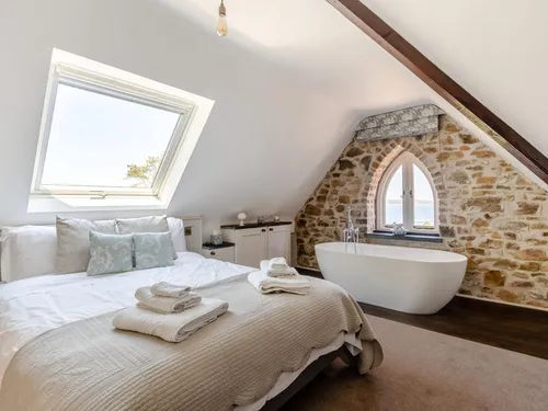 Bedroom with freestanding bath and stone feature wall under sloped ceiling
