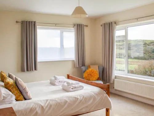 Cottage bedroom with double bed, windows and armchair with orange cushion