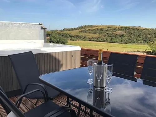 Cottage deck with glass table, chairs and hot tub overlooking fields