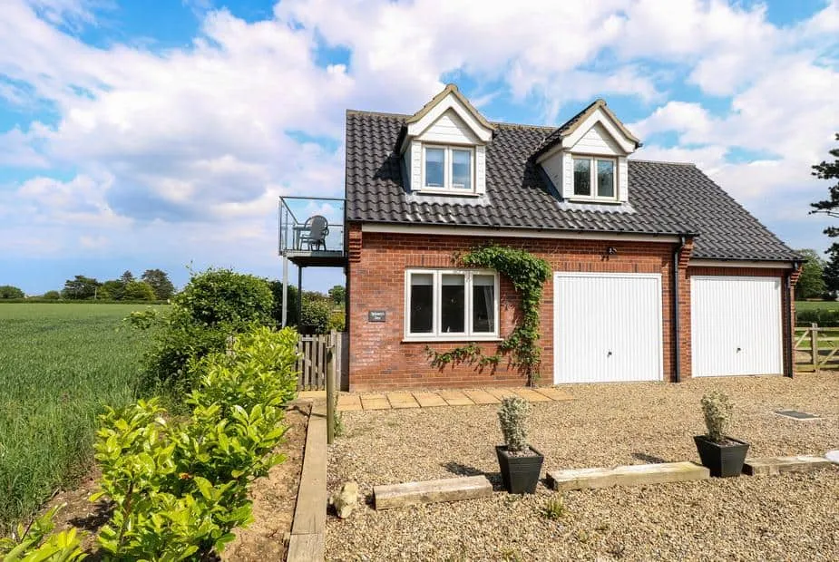 Spinney's Den red-brick cottage with balcony overlooking fields and gravel driveway