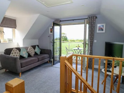 Cottage lounge with sofa, TV and patio doors opening to balcony with table and chairs