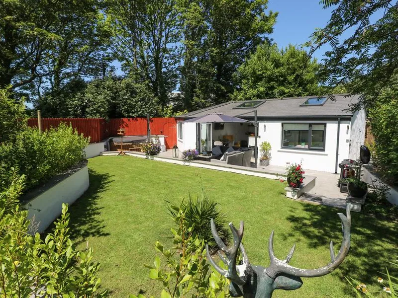 Summerhouse with patio seating, umbrella, and enclosed garden lawn surrounded by trees