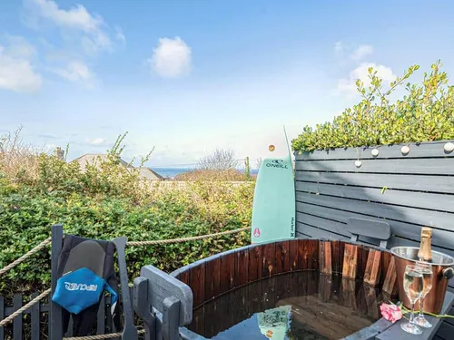 Cottage garden hot tub with surfboard and champagne, partial sea view in background