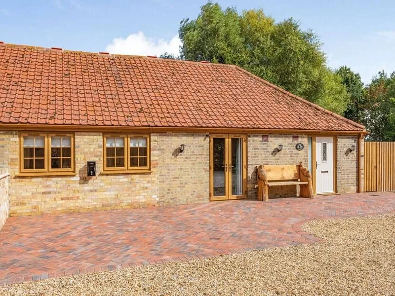 Tawny Acre Barn brick cottage exterior with tiled roof and wooden bench by entrance.